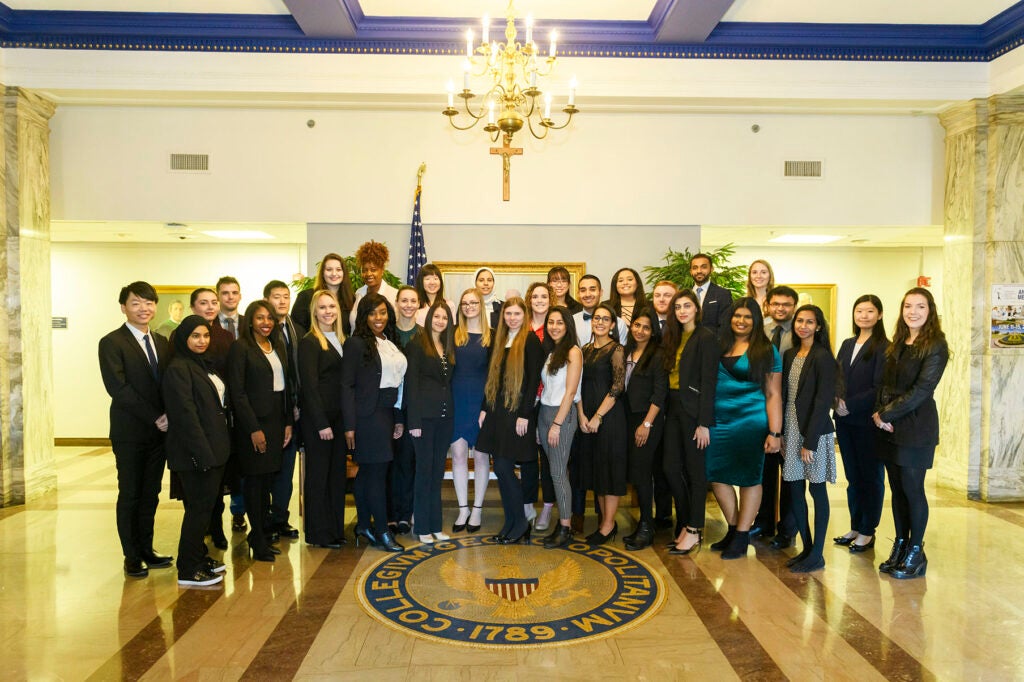 Students, faculty and staff pose around a Georgetown seal inlaid in the floor, in Fall 2018