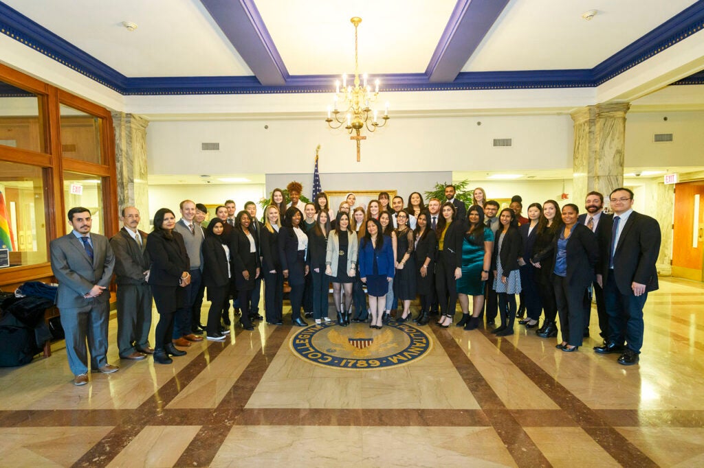 Students, faculty and staff pose around a Georgetown seal inlaid in the floor, in Fall 2018
