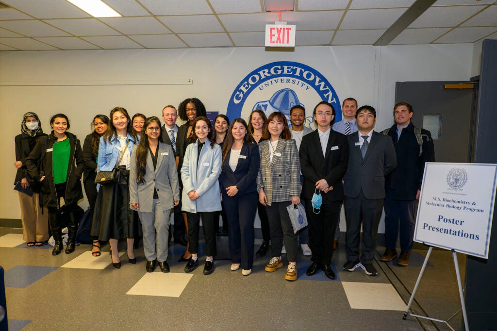 Students pose together in the Preclinical Building in Spring 2022, behind a sign for poster presentations